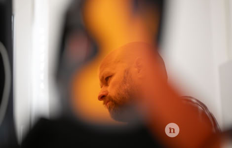 Verschwommenes Bild eines Mannes mit Glatze, der durch eine orangefarbene Form teilweise verdeckt ist.